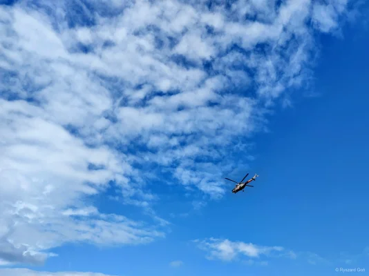 Helikopter w locie na tle błękitnego nieba z białymi chmurami.