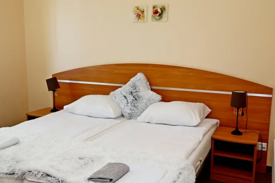 Sypialnia z dwuosobowym łóżkiem, białą pościelą, puszystą poduszką i drewnianym wezgłowiem.