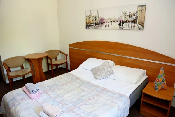 Sypialnia z szerokim drewnianym wezgłowiem i białą pościelą; na ścianie panorama Cambridge z różowym kwitnącym drzewem.