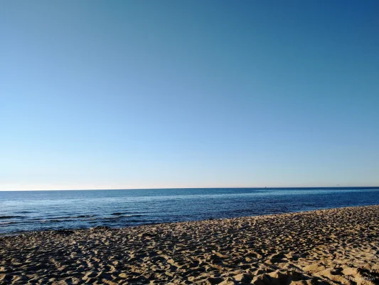 Szeroka, piaszczysta plaża w Rewalu z delikatnymi śladami stóp na piasku, spokojne morze i bezchmurne niebo.